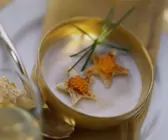 Cremefarbene Suppe in goldener Schale, garniert mit Schnittlauch, Toaststernen und Kaviar