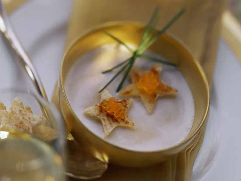 Cremefarbene Suppe in goldener Schale, garniert mit Schnittlauch, Toaststernen und Kaviar
