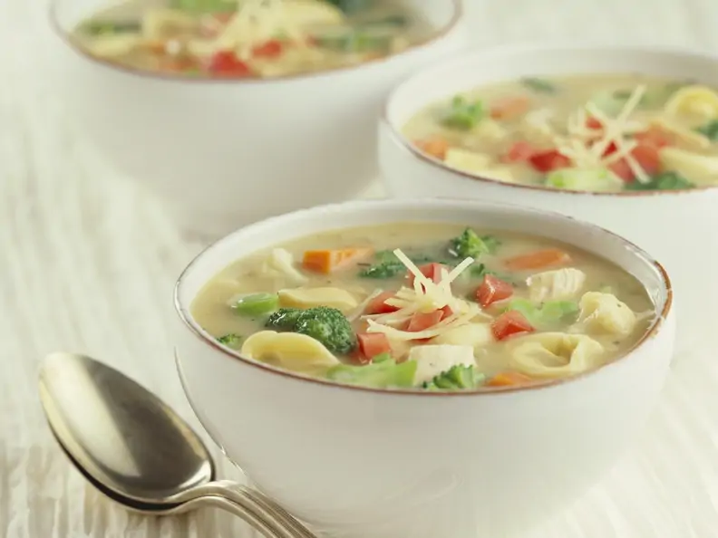 Drei weiße Schälchen gefüllt mit bunter Gemüsesuppe und Tortellini