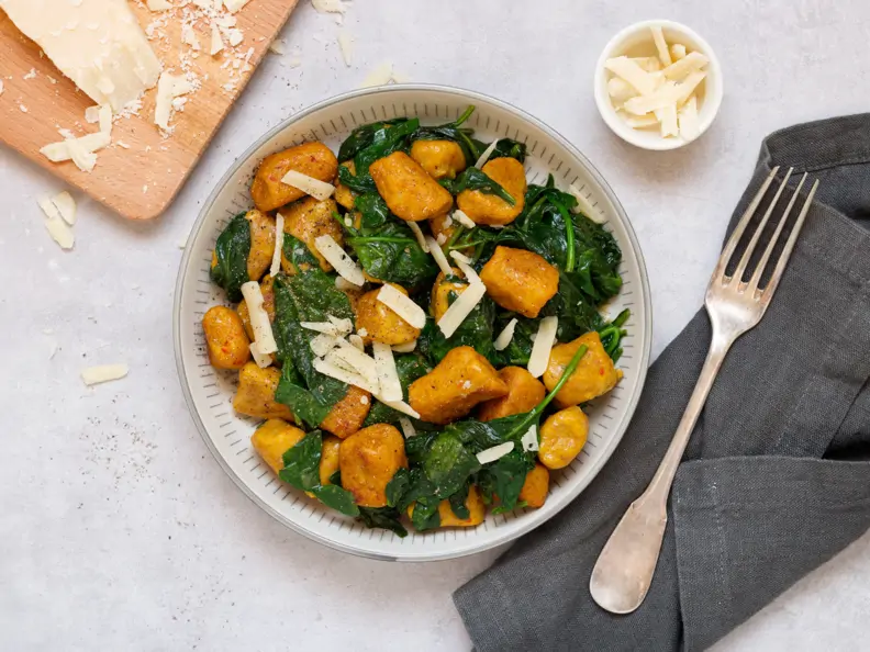 Kürbisgnocchi mit Spinat, daneben Gabel und Parmesan