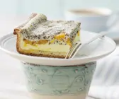 Ein Stück Käsekuchen mit Mohnbelag auf weißem Teller