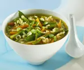 Gemüsesuppe mit Spargel und Reis in Schale neben weißem Löffel