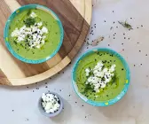 Grüne Suppe in zwei Schalen mit weißem Topping