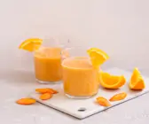 Oranger Smoothie im Glas mit Orangenviertel am Glasrand.