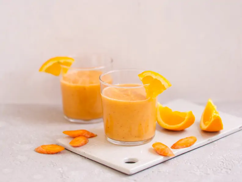 Oranger Smoothie im Glas mit Orangenviertel am Glasrand.
