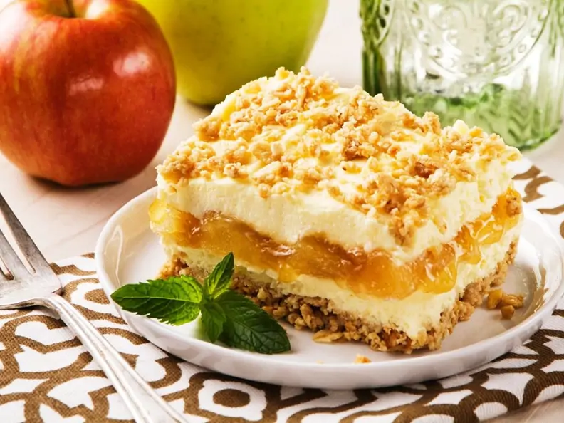 Geschichteter Apfel-Käsekuchen mit Knuspermüsli auf weißem Teller