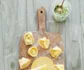 Tortellini auf bemehltem Brett neben Pestoglas mit Löffel