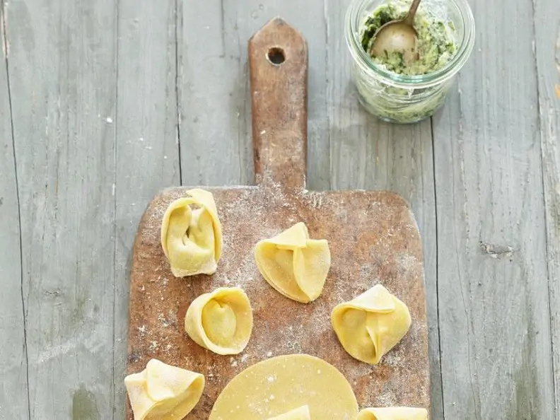 Tortellini auf bemehltem Brett neben Pestoglas mit Löffel