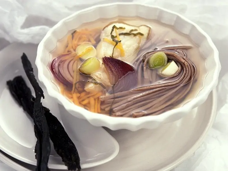 Gemüsesuppe in weißer Schale mit Nudeln und Fisch